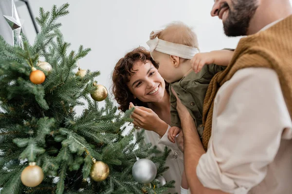 Bearded father holding infant daughter near decorated christmas tree and happy wife — Stock Photo