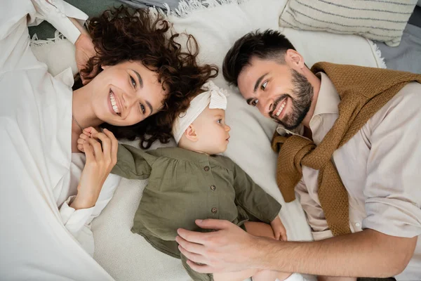 Вид веселых родителей, лежащих на кровати с девочкой — стоковое фото