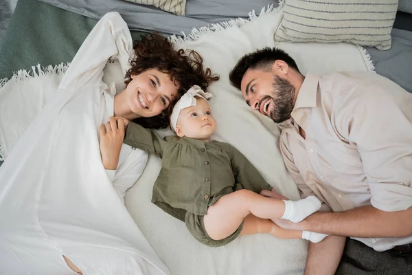 Vista superior de los padres positivos con niña acostada en la cama en casa - foto de stock
