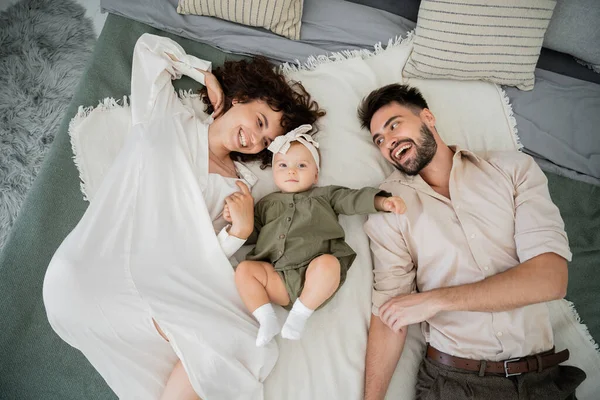 Vista dall'alto di genitori felici e neonata sdraiata sul letto a casa — Foto stock