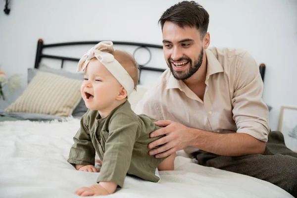 Happy bearded father looking at infant baby crawling on bed — Stock Photo