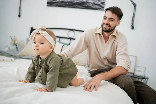 Cheerful and bearded father looking at infant baby crawling on bed — Stock Photo