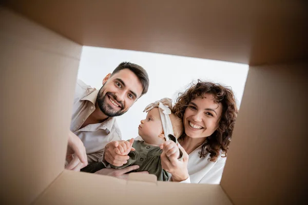 Bottom view of happy parents holding infant baby girl and looking inside of carton box — Stock Photo