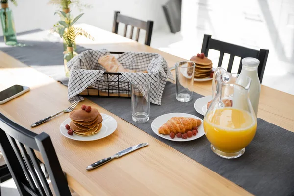 Panquecas saborosas perto de croissants assados, bebidas e smartphones com tela em branco na mesa — Fotografia de Stock