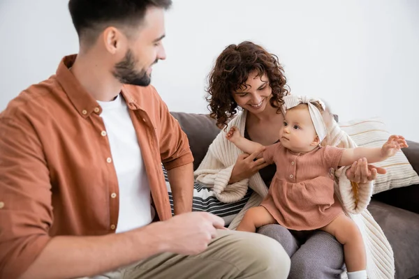 Alegre madre celebración infantil hija cerca barbudo marido sentado en sofá — Stock Photo