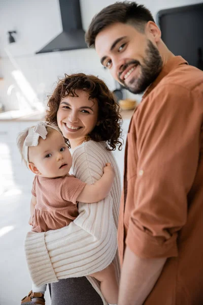 Веселая мать держит младенца малышку рядом улыбающийся муж дома — стоковое фото