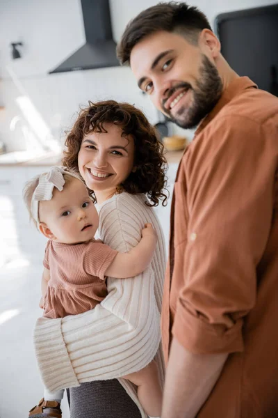 Mãe alegre segurando bebê bebê menina perto sorrindo marido em casa — Fotografia de Stock