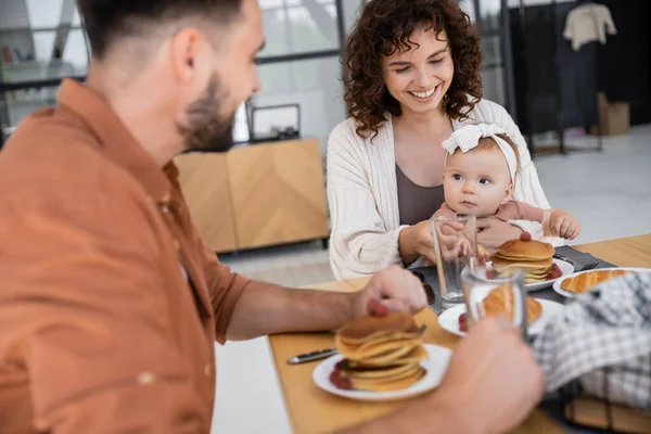 Mujer feliz sosteniendo hija bebé y desayunando con el marido - foto de stock