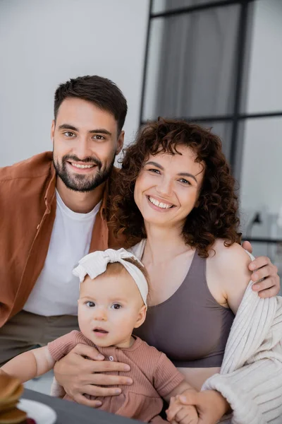 Fröhliche Familie mit kleiner Tochter schaut zu Hause in die Kamera — Stockfoto