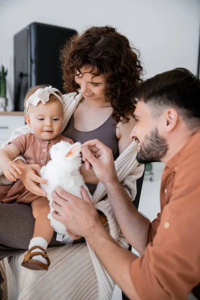 Felice uomo barbuto tenendo morbido giocattolo vicino figlia del bambino e moglie allegra — Foto stock