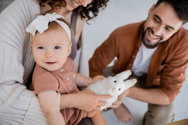 Vista de ángulo alto de niña feliz sonriendo cerca de los padres con juguete suave - foto de stock