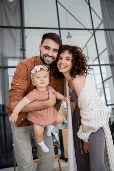 Feliz pai barbudo segurando nos braços bebê filha perto alegre esposa em casa — Fotografia de Stock