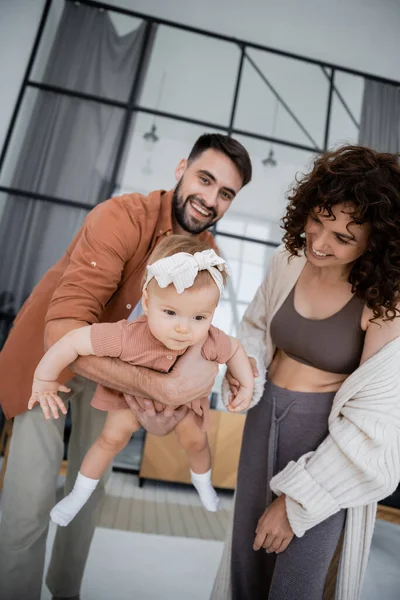Positive bearded father holding in arms baby daughter near cheerful wife at home — Stock Photo