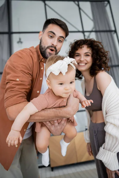 Excited bearded father holding in arms baby daughter near cheerful wife at home — Stock Photo