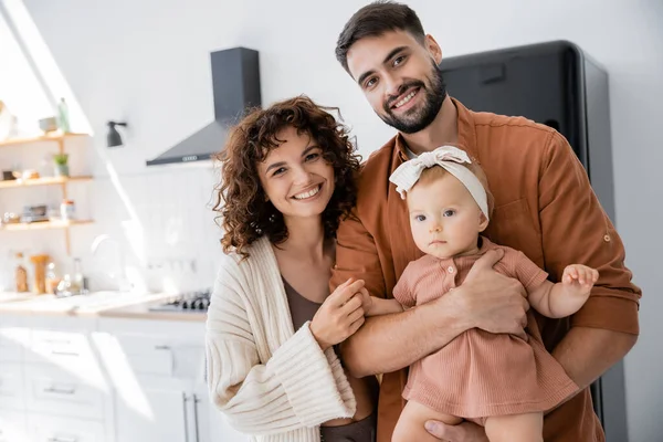 Alegre mujer de pie cerca barbudo marido celebración en brazos bebé hija - foto de stock