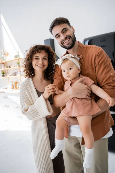 Gioiosa donna in piedi vicino barbuto marito tenendo in braccio bambino figlia in abito — Foto stock