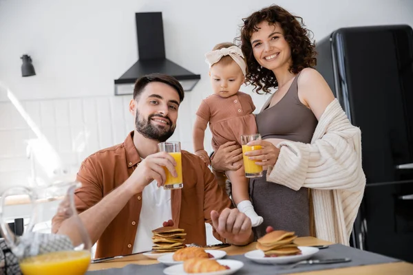 Alegre mujer sosteniendo en brazos infantil hija cerca de marido durante el desayuno - foto de stock