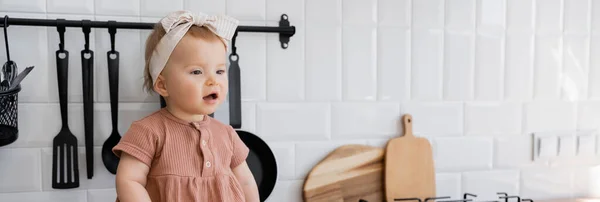 Niña sorprendida en diadema y vestido rosa sentado cerca de tablas de cortar, pancarta - foto de stock