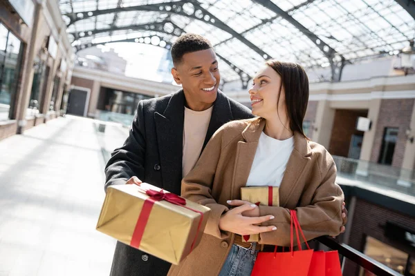 Homme afro-américain à la mode donnant un cadeau de nouvelle année à petite amie heureuse avec des sacs à provisions — Photo de stock