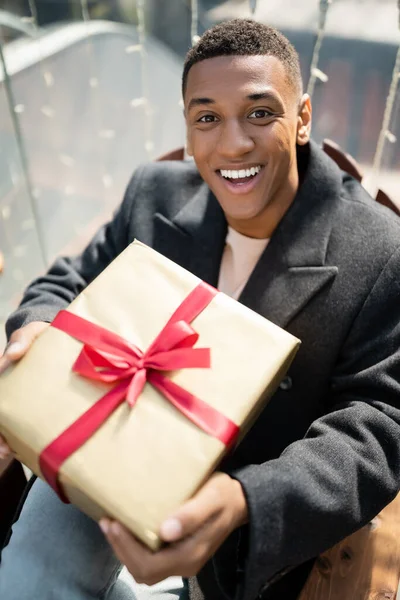 Возбужденный африканский американец с подарочной коробкой смотрит в камеру на улице — стоковое фото
