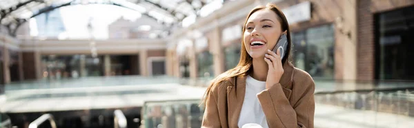 Young excited woman talking on mobile phone on blurred street, banner — Stock Photo