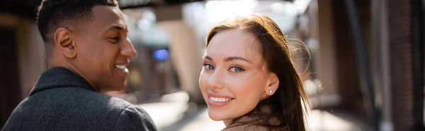 Joyful woman smiling at camera near stylish african american man on blurred background, banner — Stock Photo