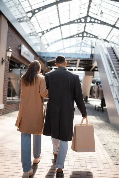 Visão traseira do homem americano africano com sacos de compras andando com namorada morena na rua urbana — Fotografia de Stock