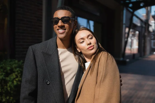 Pleased woman looking away near smiling african american boyfriend in sunglasses — Stock Photo
