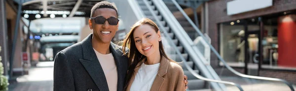 Uomo afroamericano in occhiali da sole e giovane donna alla moda guardando la fotocamera sulla strada urbana, banner — Foto stock