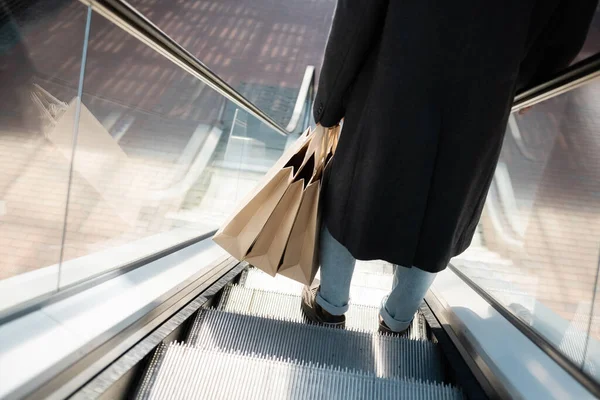 Visão de alto ângulo do homem cortado no casaco segurando sacos de compras na escada rolante — Fotografia de Stock