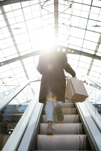 Vista posteriore dell'uomo afro-americano con borse della spesa che camminano sulla scala mobile sotto il sole — Foto stock