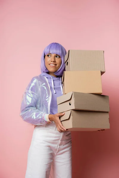 Happy african american woman in purple wig holding carton boxes on pink — Stock Photo