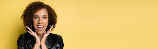 Femme afro-américaine étonnante en veste en cuir élégant geste isolé sur jaune, bannière — Photo de stock