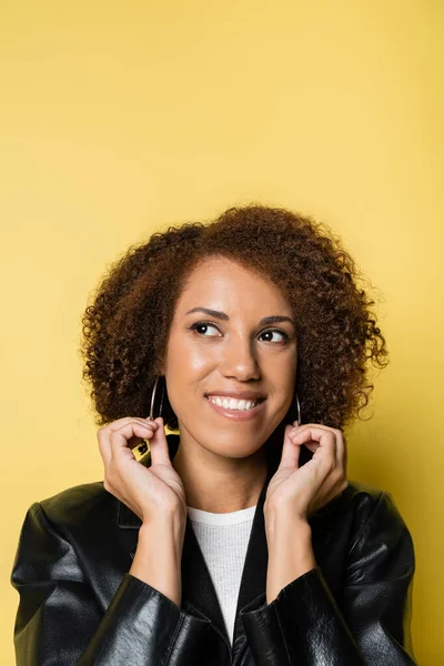 Pleased african american woman in stylish leather jacket looking away on yellow — Stock Photo