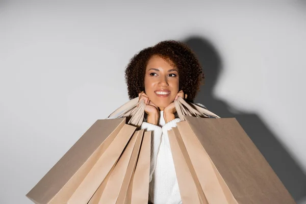 Encantada mulher afro-americana sorrindo e segurando sacos de compras em cinza — Fotografia de Stock