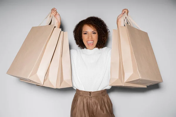 Femme afro-américaine étonnante en tenue automnale tenant des sacs à provisions sur gris — Photo de stock