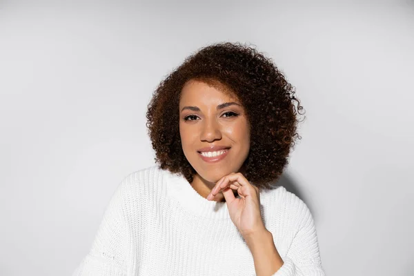 Portrait of happy and curly african american woman smiling on grey background — Stock Photo