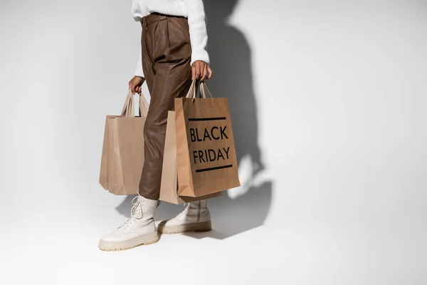 Cropped view of african american woman in autumnal outfit holding shopping bags with black friday lettering on grey — Stock Photo