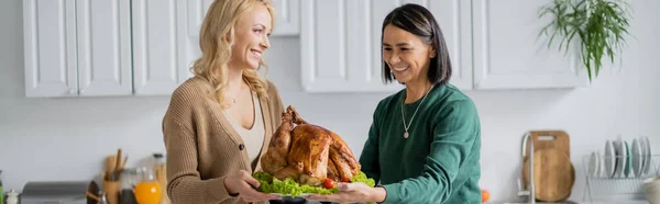 Multiethnic woman holding thanksgiving turkey with daughter at home, banner — Stock Photo