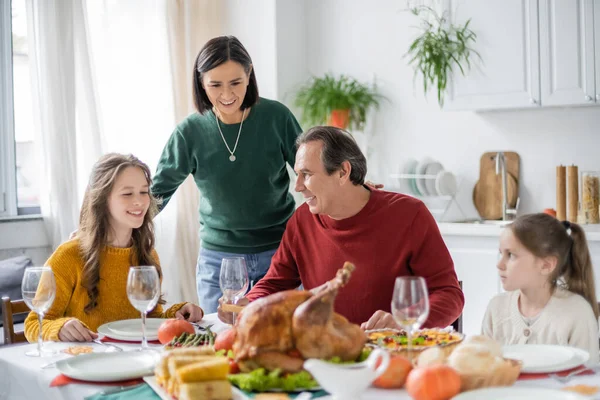 Smiling multiethnic grandparents and grandchildren sitting near blurred thanksgiving dinner at home — Stock Photo