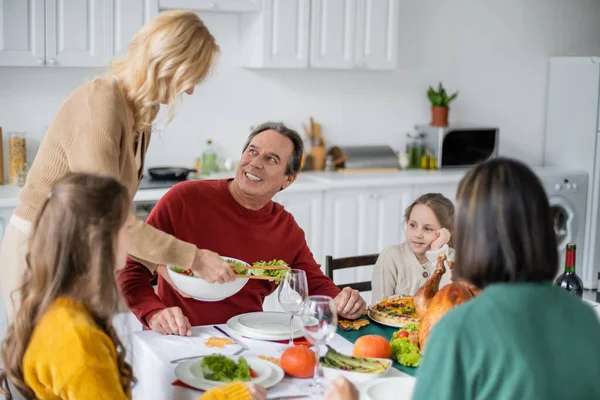 Donna che tiene l'insalata vicino a genitori e figlia durante la cena del Ringraziamento a casa — Foto stock