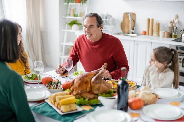 Avô sênior conversando com a família perto do jantar de ação de graças borrado em casa — Fotografia de Stock