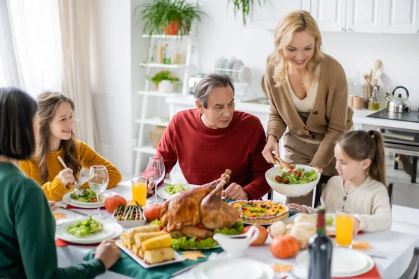 Mujer sonriente sosteniendo ensalada cerca de la hija y la familia durante la cena de acción de gracias — Stock Photo