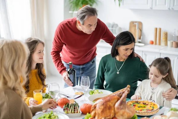 Abuelos multiétnicos mirando al niño cerca de la familia y la cena de acción de gracias en casa - foto de stock