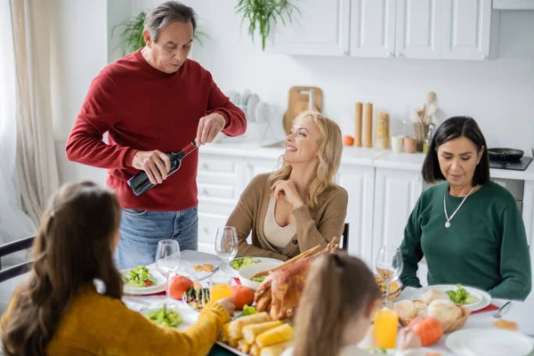 Lächelnde Frau betrachtet Eltern mit Wein in der Nähe von Danksagungsessen und multiethnischer Familie zu Hause — Stockfoto