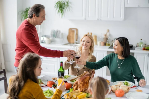 Brindisi multiculturale in famiglia con vino vicino ai bambini sfocati durante la festa del Ringraziamento a casa — Stock Photo