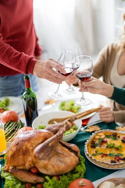 Vista recortada de tostadas familiares con vino cerca de la deliciosa cena de pavo y acción de gracias en casa - foto de stock