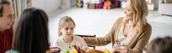 Mother looking at child near family and dinner during thanksgiving celebration, banner — Stock Photo