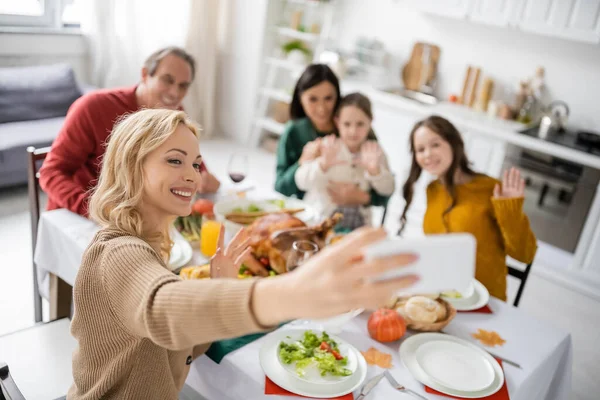 Donna sorridente che prende selfie con la famiglia offuscata vicino alla cena del Ringraziamento a casa — Foto stock