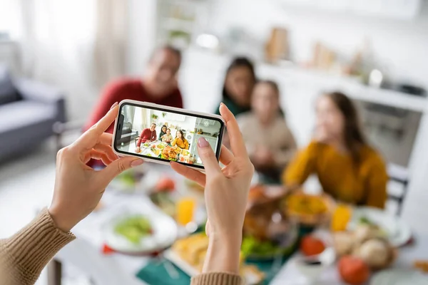 Mujer tomando fotos de la familia multiétnica cerca de la cena de acción de gracias en casa - foto de stock